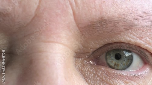 mature female face woman 50-55 years old, looks examines wrinkles around eyes, skin age-related changes, care anti-aging procedures