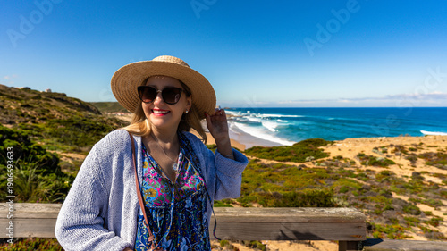 Happy mature woman tourist standing at viewpoint to Monte Clerigo beach on Algarve coast on sunny spring day. Front view