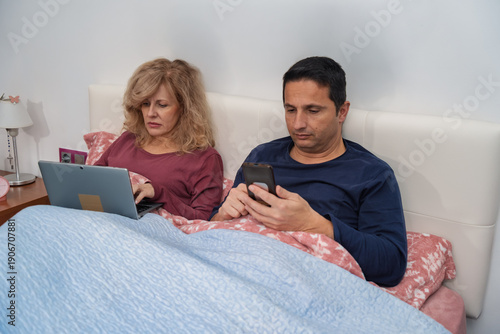 Couple ignoring each other in bed using technology