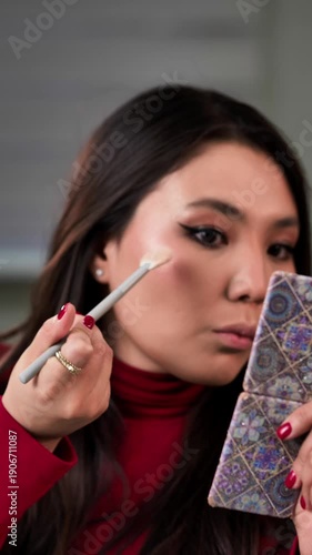 Close-up of a young woman applying highlighter to her face, creating a radiant and glowing makeup look.