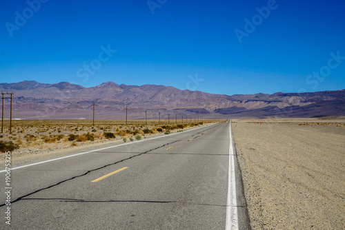 Fotografie Empty desert highway stretching into the distance with mountains under clear blue sky