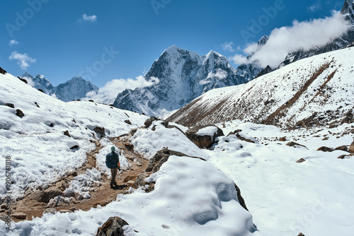 Alone backpacker confidently walks along mountain trail Everest Base Camp in Nepal with majestic snow-capped peaks of Himalayas in background.