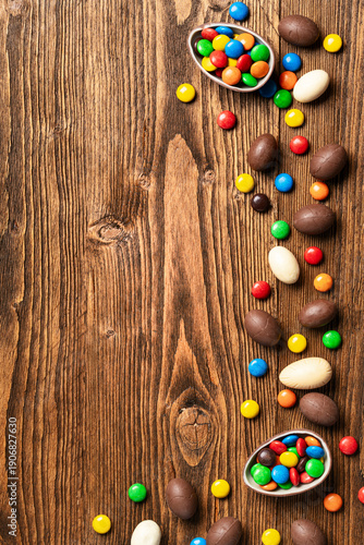 Easter chocolate eggs and colorful candies border on wooden background with copy space