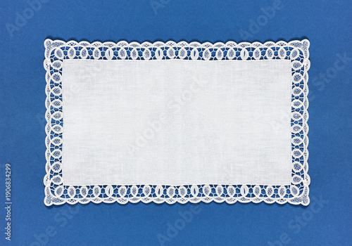 A rectangular white tablecloth with an openwork lace border on a blue background. Empty space for text. Close-up, top view, copy space, flat lay, collage, banner, mock up, blank