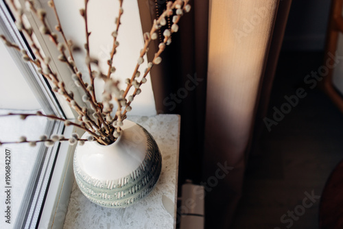 Fotografie Pussy willow branches in a ceramic vase on a windowsill with warm natural light