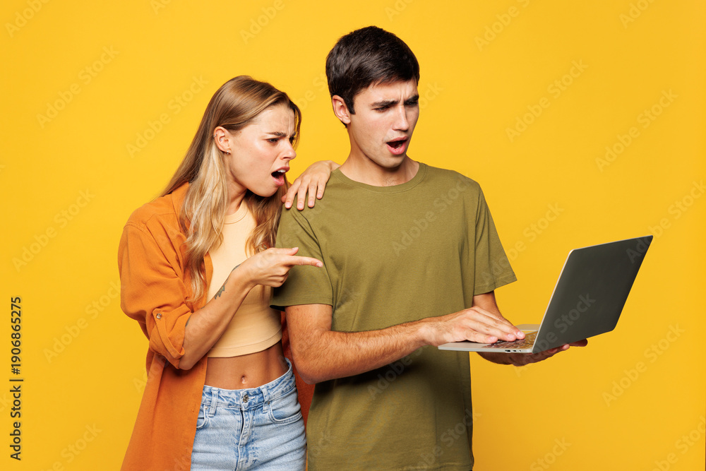 Fototapeta premium Young sad couple two friends family IT man woman wears casual clothes hold use work point finger on laptop pc computer together isolated on pastel plain light yellow color background studio portrait.