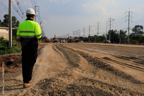 Φωτογραφία Civil engineer in reflective safety vest and helmet monitoring road construction site, coordinating machinery, traffic control, and utility infrastructure along expanding highway corridor
