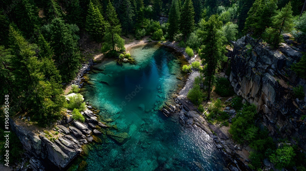Fototapeta premium Aerial drone view captures a crystal clear heart-shaped turquoise lake nestled in a lush green pine forest with dramatic cliffs and ripples.
