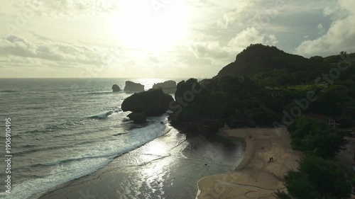 Aerial view of the beautiful Siung Beach coastline with lush green hills meeting the crashing waves, Gunungkidul Regency, Special Region of Yogyakarta, Indonesia.