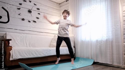 Caucasian boy doing an exercise Jumping Jacks on yoga mat at home. Children workout. Morning warmup. Child strengthening the muscles of legs, endurance and balance. Strong sporty body. HQ 4k footage.