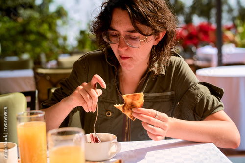 A woman with glasses enjoying breakfast or brunch outdoors, surrounded by greenery and sunlight. Kigali, Rwanda