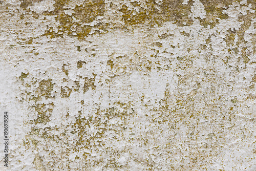Close-up of a heavily weathered wall with peeling white paint revealing rough yellow-brown stucco, creating a textured, grunge-style background conveying age, decay, and urban wear