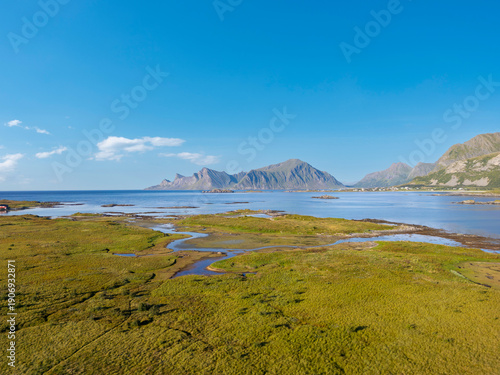 Aerial view near Fredvang overlooking salt marshes and coastal marshland with branching tidal creeks, with the peak of Hustinden in the background. Lofoten in Norway
