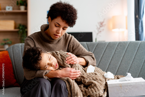 Mother comforting sick child resting on her lap at home