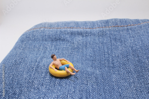 Miniature swimmer floats on inflatable ring over denim