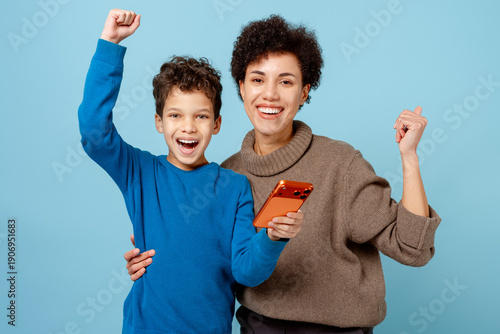 Mother and son celebrating success online with smartphone on blue background