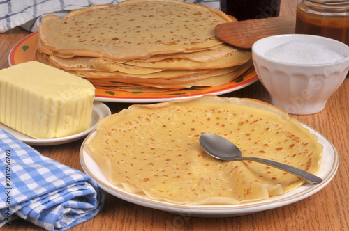 Crêpe dans une assiette avec une cuillère et du sucre, du beurre et du caramel au second plan