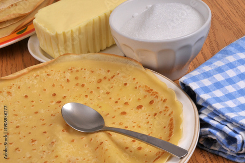Crêpe dans une assiette avec une cuillère, du beurre et du sucre en poudre au second plan