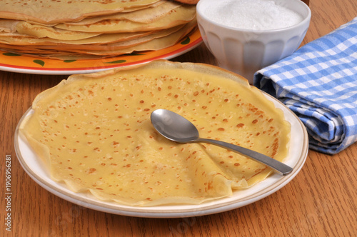 Crêpe dans une assiette avec une cuillère et du sucre en poudre au second plan