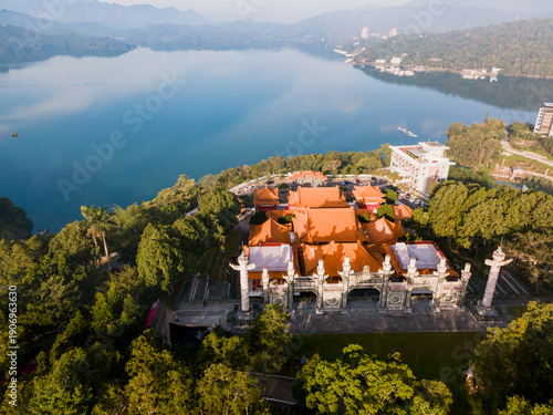 Aerial view of Wen Wu Temple overlooking Sun Moon Lake in Taiwan on a sunny morning, with traditional Chinese architecture set against blue water, forested hills, and clear skies.

