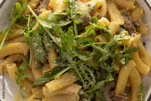 Close up pasta with arugula parmesan. Penne tossed with crumbled beef, cherry tomato and shaved parmesan, finished with light oil and pepper rustic ceramic bowl, warm tones, visible steam and textured