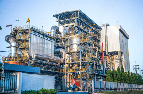 Fotografie Modern industrial power plant with complex piping and steel structures under a clear sky