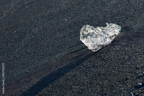 A crystal‑clear shard of ice glows against the dark volcanic sand of Diamond Beach near Jökulsárlón glacier lake as soft sunrise light stretches across Southern Iceland’s rugged shoreline