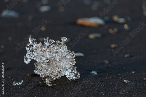 A crystal‑clear shard of ice glows against the dark volcanic sand of Diamond Beach near Jökulsárlón glacier lake as soft sunrise light stretches across Southern Iceland’s rugged shoreline