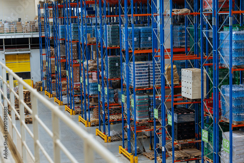 Obraz na plátně Industrial warehouse with tall blue racks and stacked pallets in a busy logistic