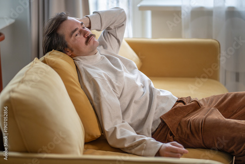 Canvastavla Exhausted man sitting on sofa staring into emptiness, deep fatigue, mental burnout, loss of energy