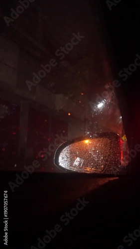 view from inside a car at night during rain, with water droplets on the window and reflections of streetlights on the rearview mirror