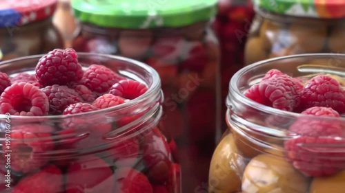 Freshly picked raspberries and preserved fruits in glass jars, a taste of summer abundance.