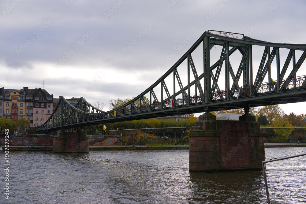 Obraz premium Scenic view of Main River with Eiserner Steg footbridge at German city of Frankfurt am Main on a cloudy autumn day. Photo taken November 3rd, 2025, Frankfurt am Main, Germany.