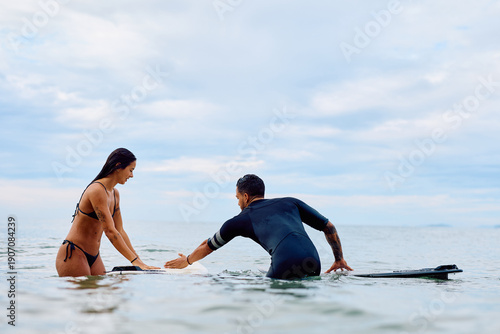 Photography Male instructor guiding female beginner on surfboard in calm ocean waters during
