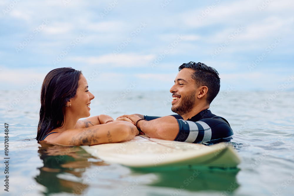 Obraz premium Happy couple interacting while lying on a surfboard in the sea, enjoying their lifestyle and summer vacation