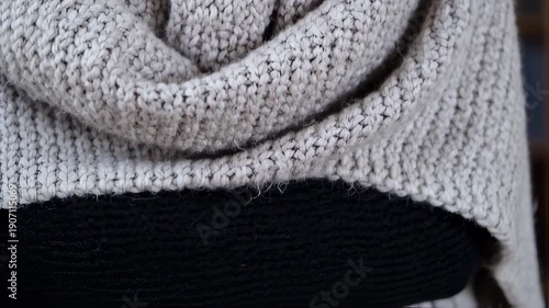 Close-up of a person wearing a cozy, light grey knitted sweater, showcasing the intricate texture and warmth of the fabric, perfect for cold weather.