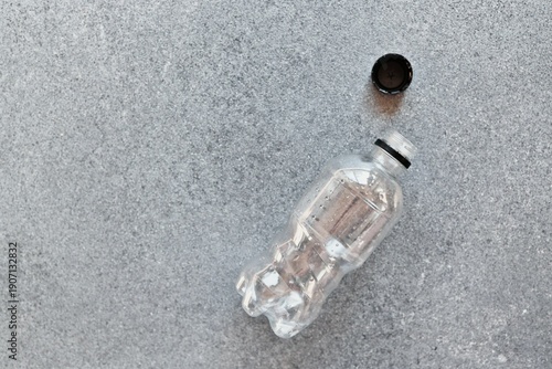 Photography Empty plastic water bottle with cap removed lying on a textured gray surface