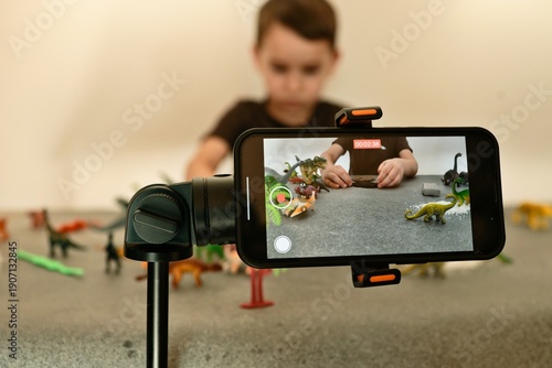 Fotografie Child filming stop motion animation with dinosaur toys on a table using a smartp