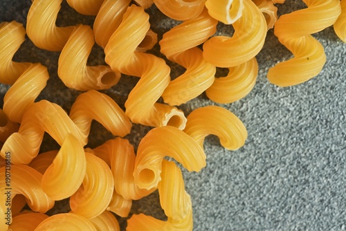 Fotografie Close-up of golden cavatappi pasta scattered on a textured grey surface