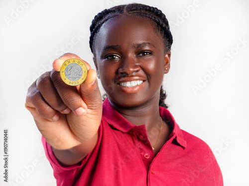 Fotografia A woman in a red polo smiles, holding a 1 Ghana Cedi coin