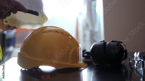 Construction worker grabbing a white hard hat from a desk with other safety equipment