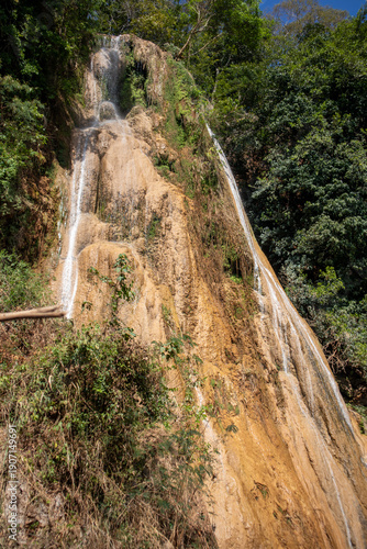 Tall Limestone Waterfall on Steep Cliff Surrounded by Tropical Forest