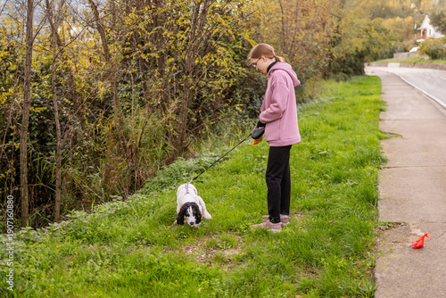 Girl picking up trash while walking a dog spaniel on a grassy path