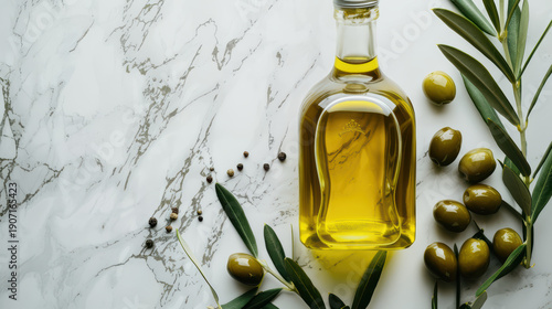 A bottle of olive oil sits on a marble countertop next to a bunch of green leave