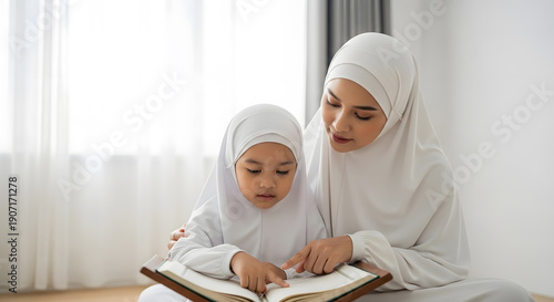 A realistic stock photo of a Muslim mother teaching her young daughter to read the Quran at home, both wearing modest white prayer clothing, child pointing at the pages of the Quran, gentle guidance a