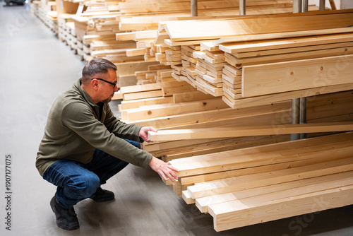 Man selecting timber or checking quality of construction lumber in hardware store