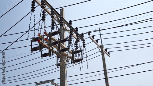 High voltage pole mounted air break switch disconnector with bird protection spiral dampers on electrical distribution line against blue sky.