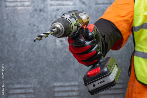Tableau sur toile Close up of a construction worker hand holding a cordless drill with drill bit on a industrial background