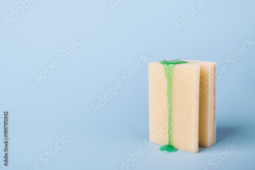 Photos Cleaning sponge with liquid dishwashing detergent dripping on light blue backgro