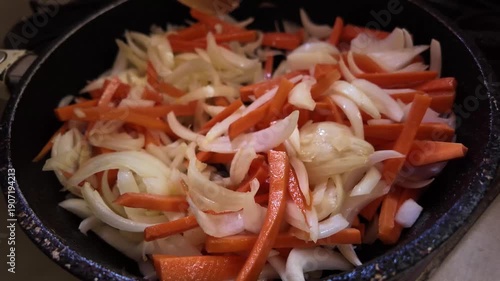 Stirring sliced onion and carrot in a hot pan